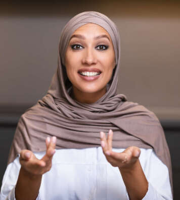 Muslim Woman Talking Looking At Camera Having Online Consultation With Dietitian Sitting In Kitchen At Home, Wearing Hijab. Video Call, Online Conference, Remote Distant Communication Concept