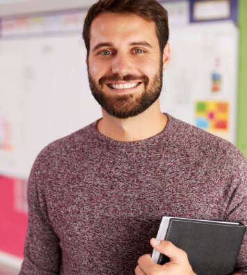 Portrait Of Male Elementary School Teacher Standing In Classroom
