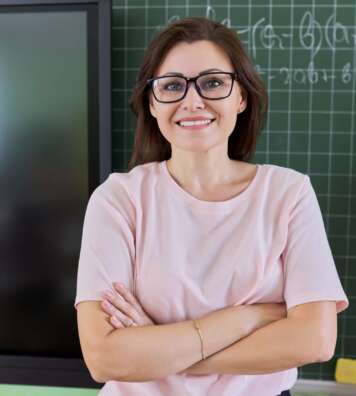 Positive confident female teacher looking at the camera with crossed arms. Green chalk board and wall digital screen background