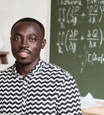 Portrait of African young teacher smiling at camera while standing in the classroom