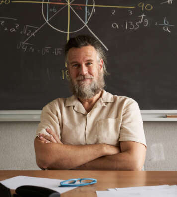 Vertical photo. Cheerful teacher looks at the camera with his arms crossed. Mathematics class.